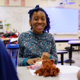 Young girl smiles at camera while diapering a doll