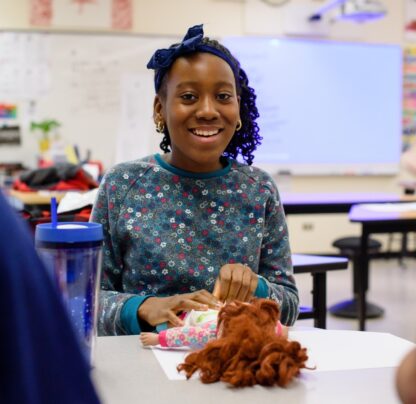 Young girl smiles at camera while diapering a doll