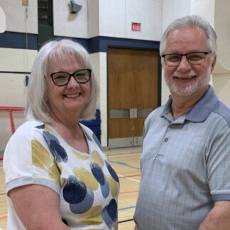 A couple holds hands facing each while looking at each other as well as the camera in a gym.