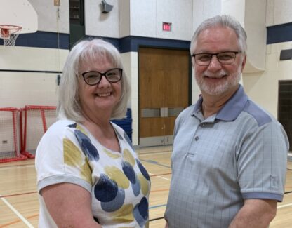 A couple holds hands facing each while looking at each other as well as the camera in a gym.