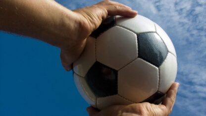 hands holding soccer ball against a blue sky