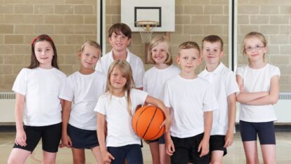 A group of kids in uniform on a basketball court facing the camera holding a basket ball and smiling.