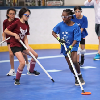 A group of teenage girls wearing safety glasses run with ringette equipment.