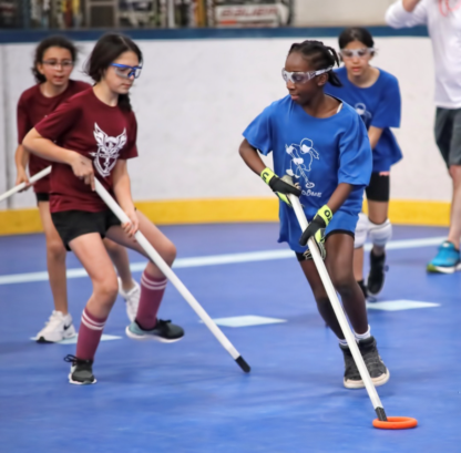 A group of teenage girls wearing safety glasses run with ringette equipment.