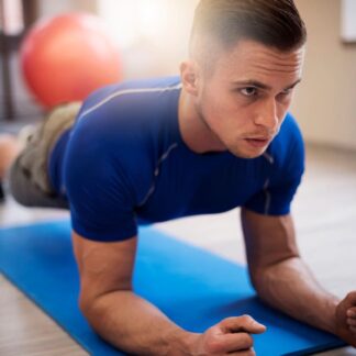 Man on yoga mat doing a plank exercise looking focused.