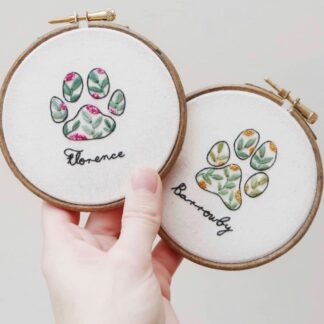 Two embroidery hoops are held to display the pawprints designs on each. One for a pet named Florence, the other is named Barrowby.