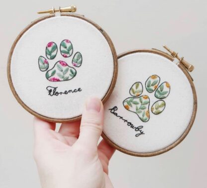 Two embroidery hoops are held to display the pawprints designs on each. One for a pet named Florence, the other is named Barrowby.