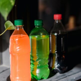 Three different coloured soda bottles sit on a shelf with liquid in each bottle.