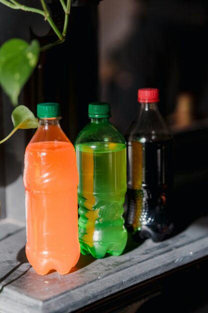 Three different coloured soda bottles sit on a shelf with liquid in each bottle.