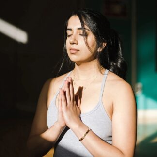 A young woman has her eyes closed in a meditative prayer pose.