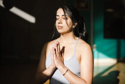 A young woman has her eyes closed in a meditative prayer pose.