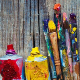 Colouful paintbrushes with open tubes of paint against a wood background