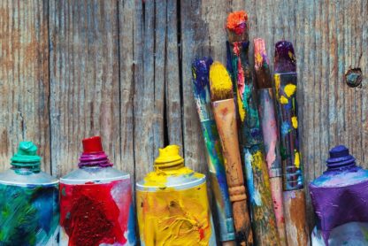 Colouful paintbrushes with open tubes of paint against a wood background