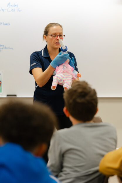 An instructor holds a doll while speaking in a CPR class