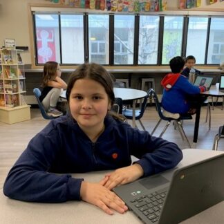 A child smiles as she works on a laptop