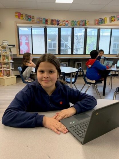 A child smiles as she works on a laptop