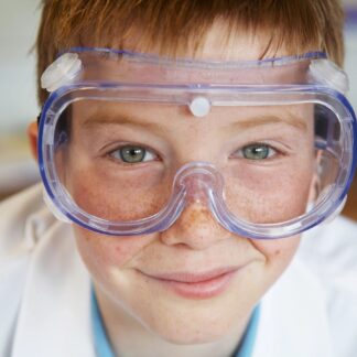 A child wearing safety glasses and a lab coat grins at the camera