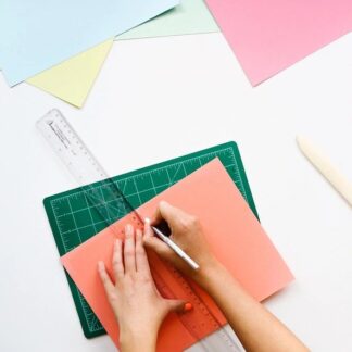 Hands use a ruler and cutting mat to cut a piece of orange paper