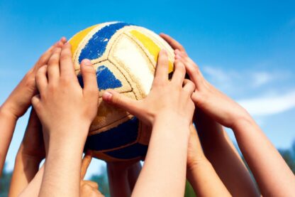 A group of hands collectively holding a volleyball in the air