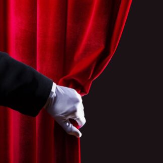 A magician's gloved hand draws back a red curtain