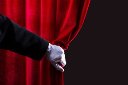 A magician's gloved hand draws back a red curtain