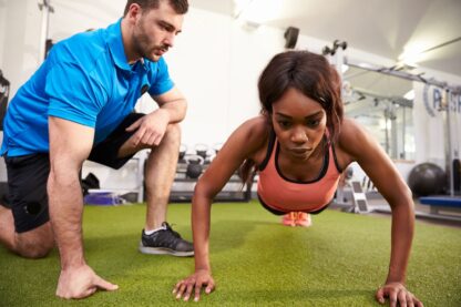 A coach works with a woman doing a pushup