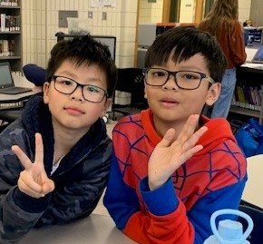 two kids with glasses wave at camera